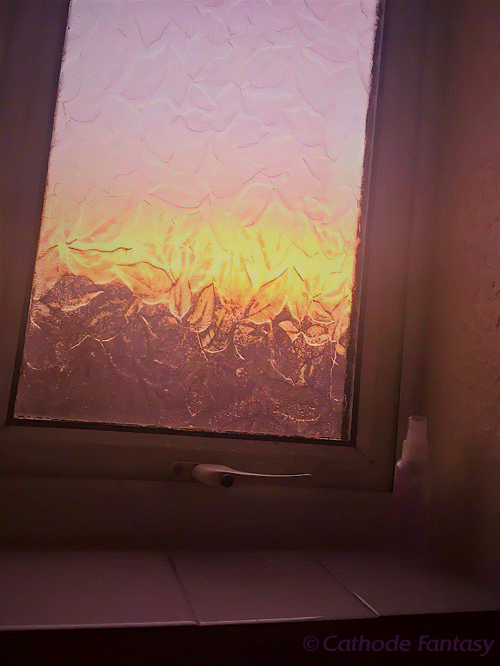 A dreamy pastel pink, yellow, and orange view of a sunrise through a frosted, leaf-textured bathroom window.